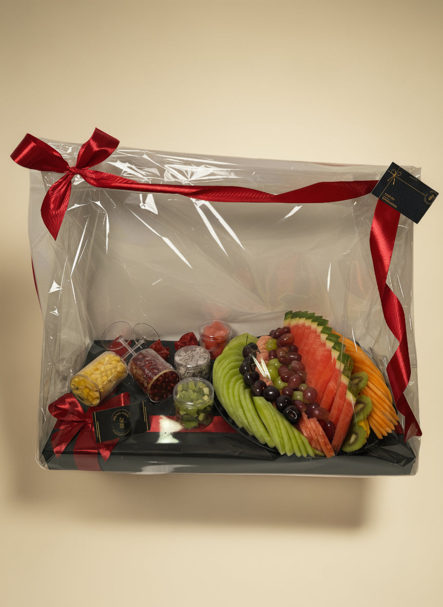 Fruit and candy arrangement in a clear box with a red ribbon on a white background