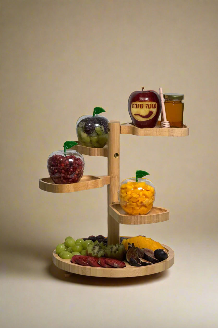 Three-tiered wooden fruit basket with various fruits and a jar on a white surface.